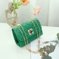 Bolso bandolera acolchado verde con cierre de trébol dorado en una mesa blanca - Celosía de diamante verde