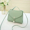 Mint green woven crossbody bag with pearl pendant and golden buckle on white cloth - Green