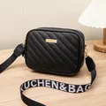 Bolso bandolera negro acolchado con correa ancha de letras sobre mesa de madera clara - Negro