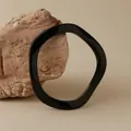 Dettaglio di un bracciale irregolare in acrilico nero poggiato su una pietra naturale - Stile Onda Nero Lucido (AB0026-6)