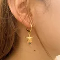 Golden turtle hoop earrings with engraved shell and green gemstone on female model - Sea Turtle With Green Stone Style (KE1779)