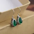 Macro view of silver vintage drop earrings with green gemstone and scrollwork details - Green