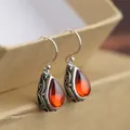 Macro shot of vintage silver teardrop earrings featuring warm orange-red gemstones - Red