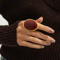 Close-up of a large oval red gemstone ring on a hand with gold polished finish metal - Gold + Red (00976)