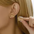 Close-up of elegant gold ribbon bow earrings worn by a model with golden hair - Gold 3D Ribbon Bow (BSSP009)