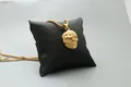 Close-up of golden skull pendant with detailed relief on a black leather cushion - Fashion Gold