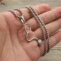 Silver stethoscope pendant necklace with thick box chain held in hand over wood - Silver
