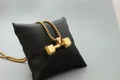 Detail einer polierten goldenen Hantel-Halskette auf einem schwarzen Schmuckkissen - Gold