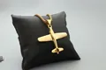 Detalle del colgante de avión dorado con cadena box pulida sobre cojín negro - Cadena de cajitas / Oro de Moda