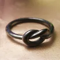 Macro view of a black stainless steel knot ring on a smooth reddish-brown satin fabric - US 6 / Black