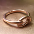 Macro shot of polished rose gold knot ring on elegant textured brown fabric - US 6 / Rose Gold