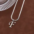 Détail du pendentif lettre F argenté avec chaîne serpent polie sur fond en daim brun - Lettre F