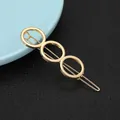 Close-up of golden geometric hair clip with three hollow rings on black leather background - Triple Linked Circles Style