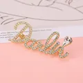 Detail van een gouden letterbroche met fonkelende steentjes en een grote druppelzirkonia - Goud
