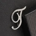 Detalle del broche de letra plateado con pedrería brillante sobre cuero negro - Letra T / Plata T