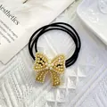 Detailed shot of a black elastic hair tie with a gold-tone pearl bow on knit texture - Hollow Pearl Bow (Style 2)