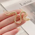 Detalle de pinza para el pelo de serpiente dorada con escamas sobre una revista - Clip de Serpiente Dorado Brillante Q009
