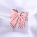 Detailed macro of a pink bow brooch with small white pearls on white fabric - Pearl Edge Bowknot / Pink
