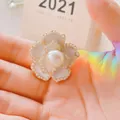 Elegant white camellia flower brooch with gold plating and pearls shown on a palm - Pearl Camellia / Camellia White