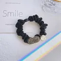 Elegante elastico per capelli in tessuto nero con strass grigi e ciondolo logo oro - Nero