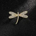 Élégante broche libellule dorée avec cristaux blancs sur fond de cuir noir texturé - Libellule Dorée