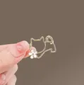 Primer plano de una pinza para el pelo dorada con forma de gato y una pequeña flor blanca - Gato Dorado