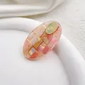 Primer plano de pinza de acetato con textura de mármol rosa y detalle de metal dorado - Redondo Rosa