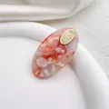 Detalle de pinza para el pelo de acetato jaspeado rosa y blanco con logo dorado oval - Redondo Rosa Multicolor