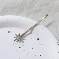 Detalle macro de un pasador de pelo dorado con pedrería brillante sobre un plato blanco - Estilo Estrella Pequeña / Oro Antiguo
