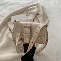 Beigefarbene Punk-Schultertasche mit silbernen Ösen und Nieten in modischer Szenerie - Gebrochenes Weiß