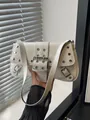 Weiße Lackleder-Baguette-Tasche mit silbernen Nieten und Schnalle in stilvoller Handhaltung - Weiß