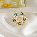 Elegante broche de corona floral con perlas y esmalte verde esmeralda sobre seda blanca - Perla Redonda