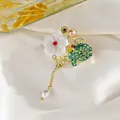 Detalle del broche de flor y mariposa con esmalte verde, perlas y borlas de cadena dorada - Mariposas Revoloteando