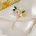 Detalle del broche de flor vintage con hojas de esmalte verde, perlas y borla colgante - Flor de ciruelo
