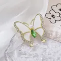 Gros plan détaillé d'une broche papillon dorée avec perles et pierres gemmes vertes - Vert