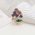 Detailed view of elegant gold brooch with purple floral crystals and green enamel leaf - Grapes