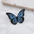 Detailed close-up of a luminous butterfly enamel pin with blue and black wing textures - Blue