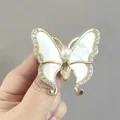 Broche papillon dorée avec ailes en nacre et strass brillants présentée à la main - Champagne