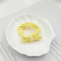 Nahaufnahme eines gelben Stoff-Haargummis mit Schleife auf einer weißen Muschelschale - Schleifenstil / Gelb