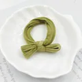 Nahaufnahme des olivgrünen Samt-Scrunchies mit Schleife in einer weißen Muschelschale - Schleifenstil / Dunkelgrün