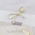 Detalle de una pinza para el cabello de metal dorado con perlas blancas y clip de pato - Lazo / Dorado