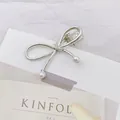 Detalle de pasador de lazo plateado con perlas sobre una revista de moda y fondo rosa - Lazo / Plateado