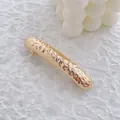 Détail d'une barrette en métal doré avec une texture martelée sur un tissu blanc - Or