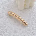 Gros plan d'une pince à cheveux en métal doré avec une texture tissée torsadée sur fond blanc - Or