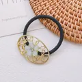 Gros plan d'un élastique à cheveux noir avec cadre floral doré et strass vert scintillant - Style Ovale Ajouré Doré (10 Élastiques à Cheveux)