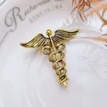 Detailed view of vintage gold Caduceus brooch with snake and wing relief on white plate - Antique Gold Caduceus Wings