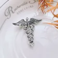 Macro shot of vintage silver Caduceus brooch with detailed wings and snakes on white ceramic - Antique Silver Caduceus Wings