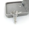 Silberne Äskulapstab-Brosche mit Flügeln auf einer grauen Samt-Schmuckschatulle - Glänzendes Silber Hermesstab Flügel