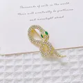Detalle de broche de serpiente dorada con cristales brillantes y ojos de gema verde - Serpiente de Oro con Diamantes Completo