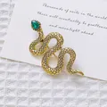Detalle macro de broche de serpiente vintage dorado con gema verde sobre fondo blanco - Serpiente de Oro Antiguo Vintage